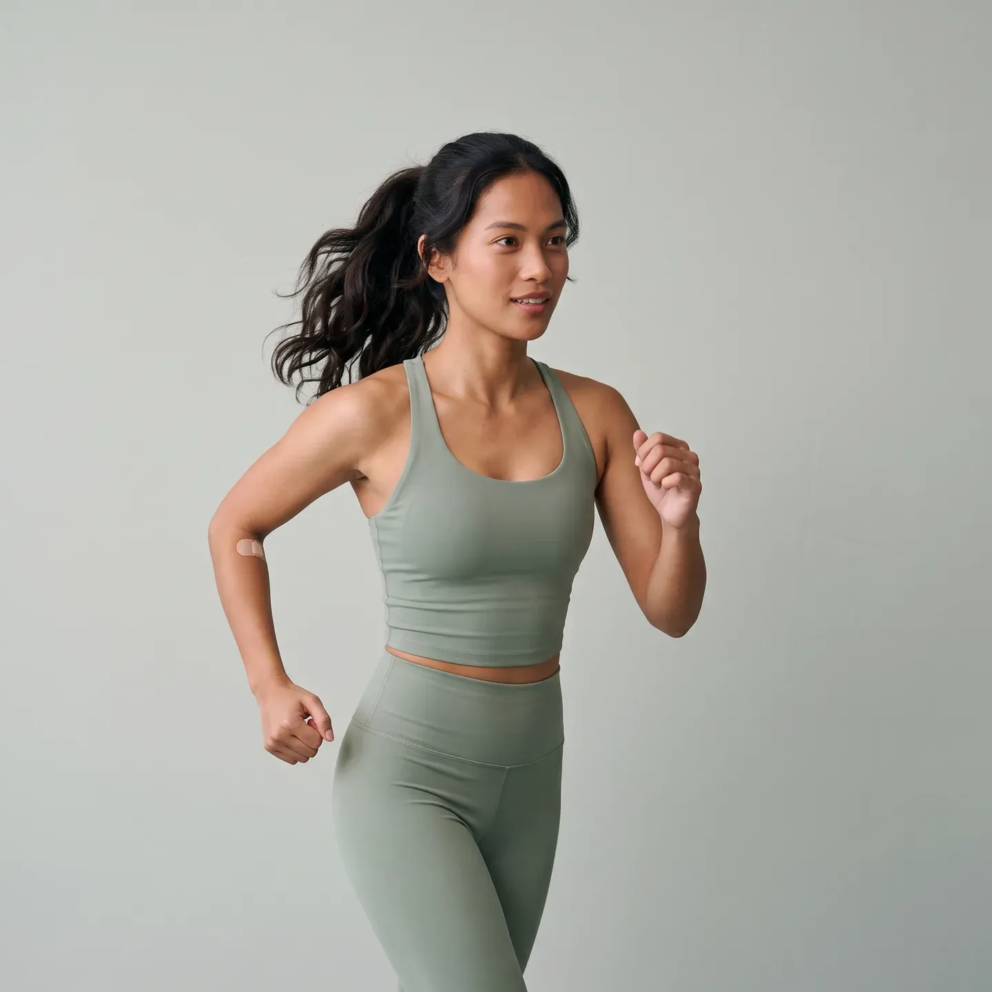 A woman in training clothes running, a small plaster on the inside of her elbow
