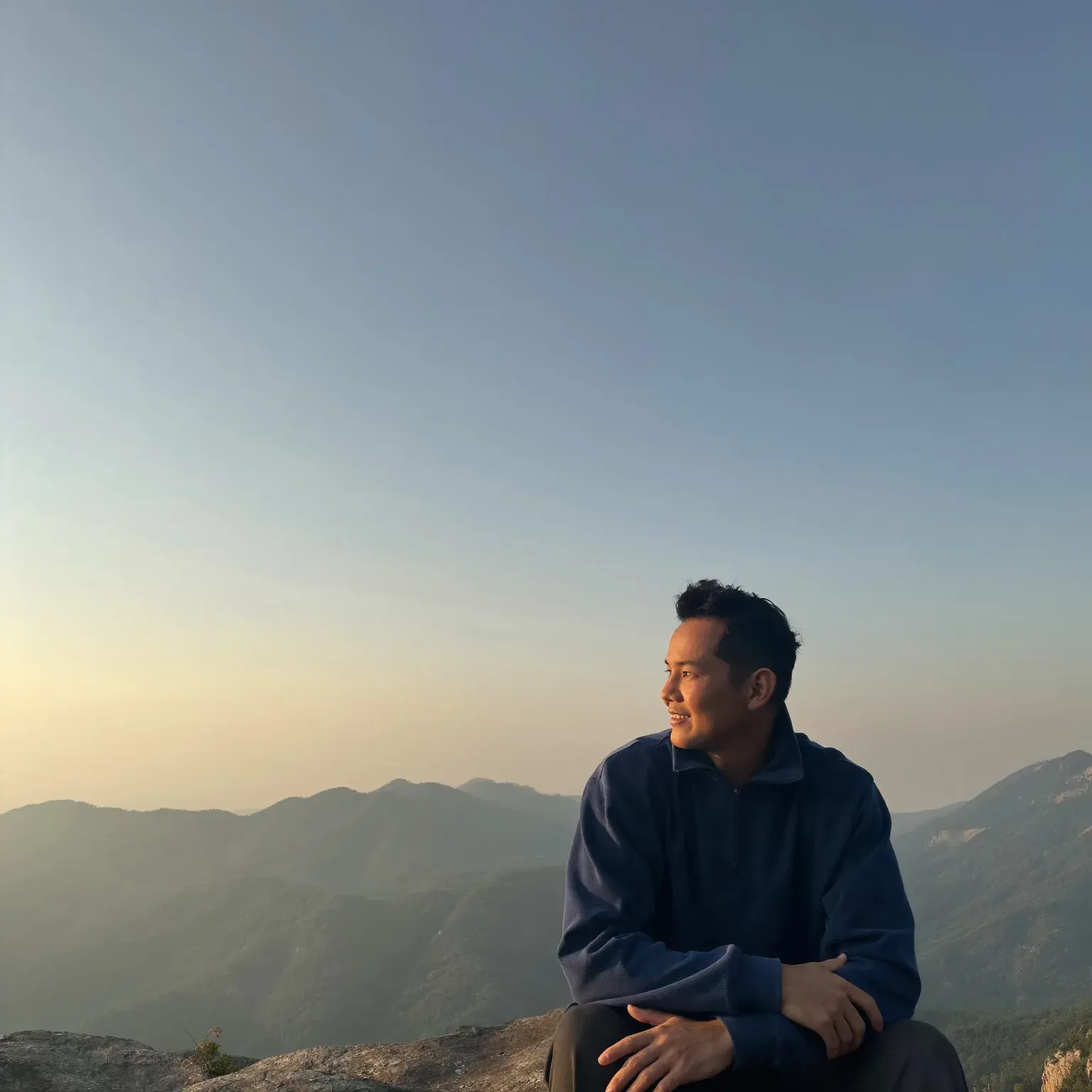 A man sitting on a rock above a mountain view