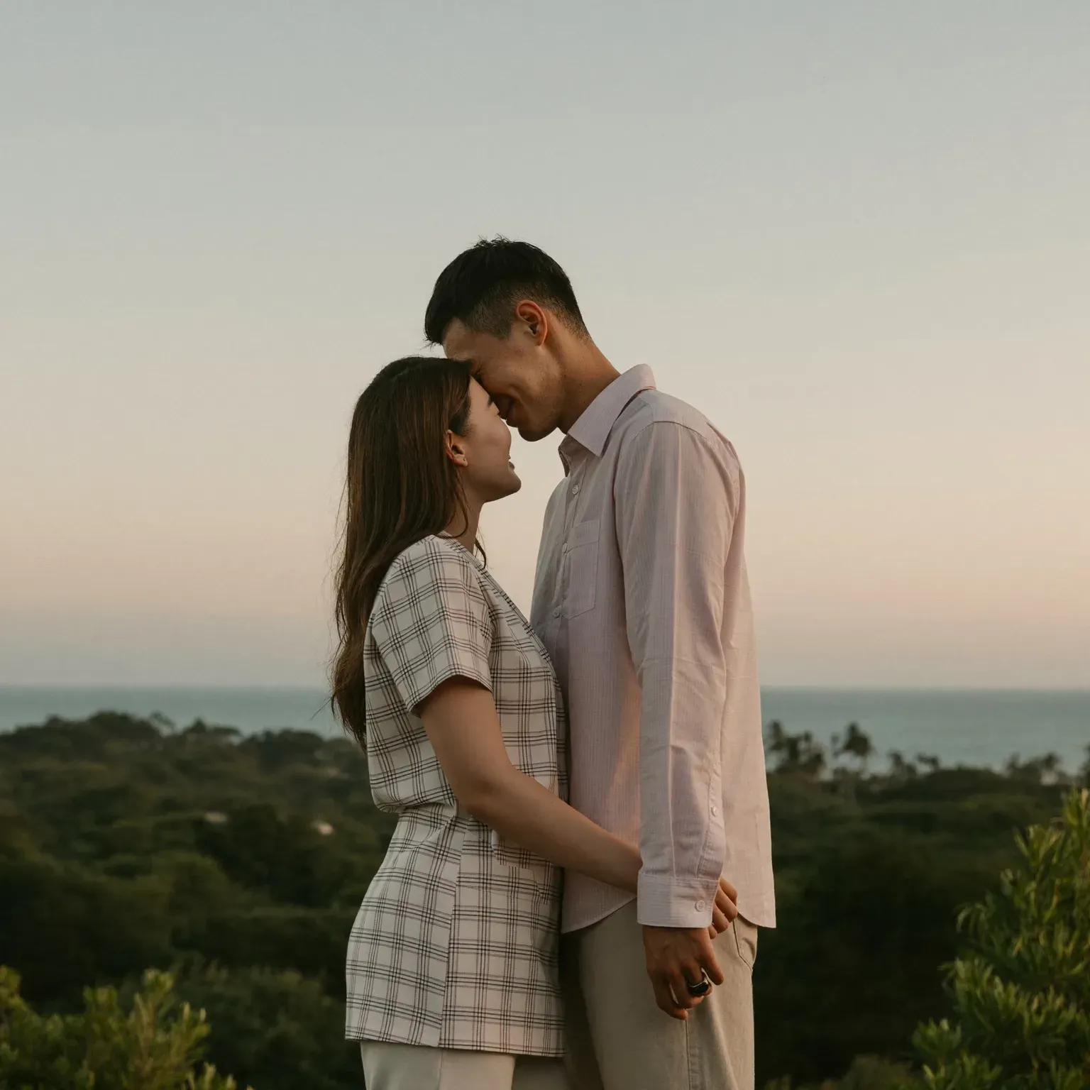 A couple standing close with their foreheads touching, at sunset