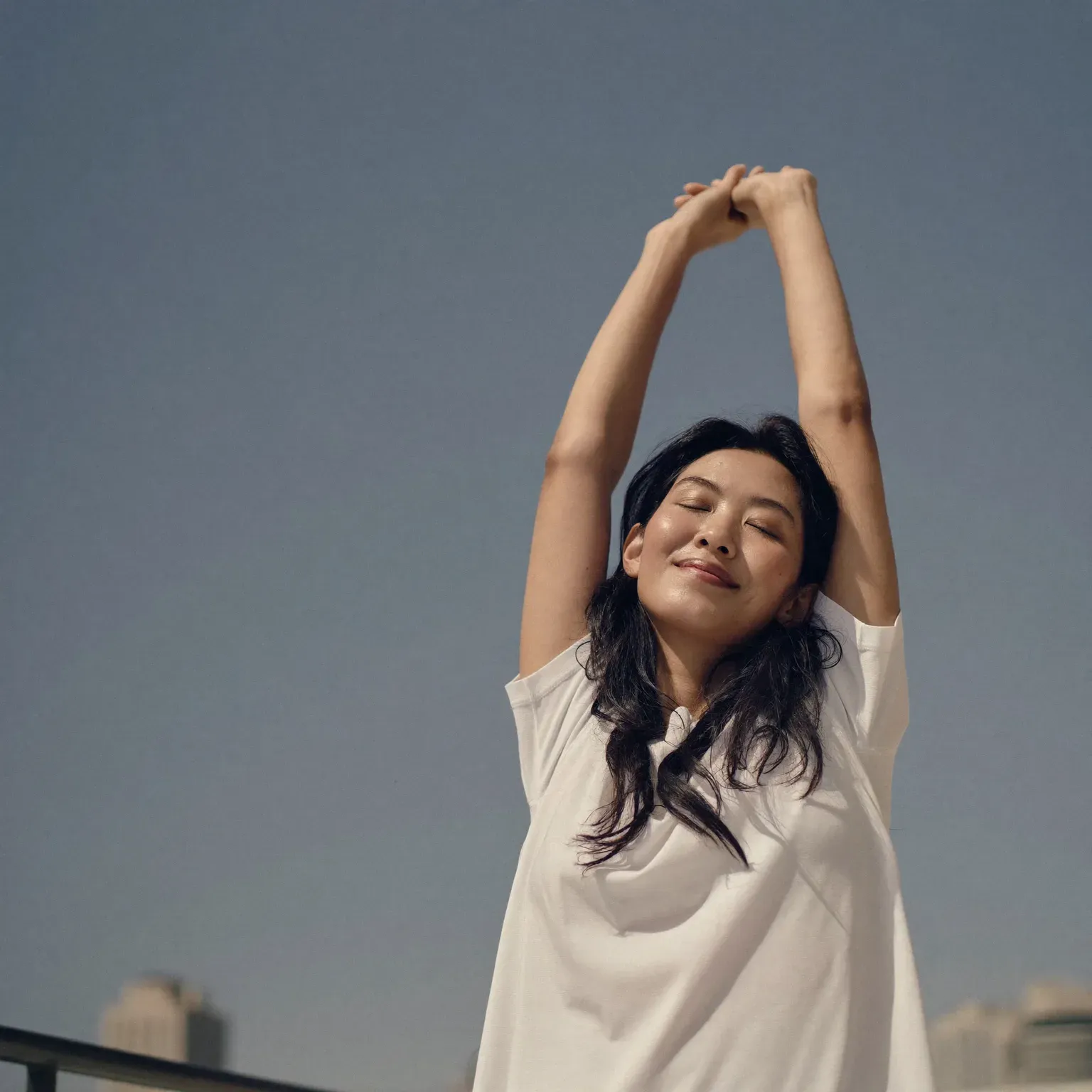 A woman stretching her arms overhead with her eyes closed