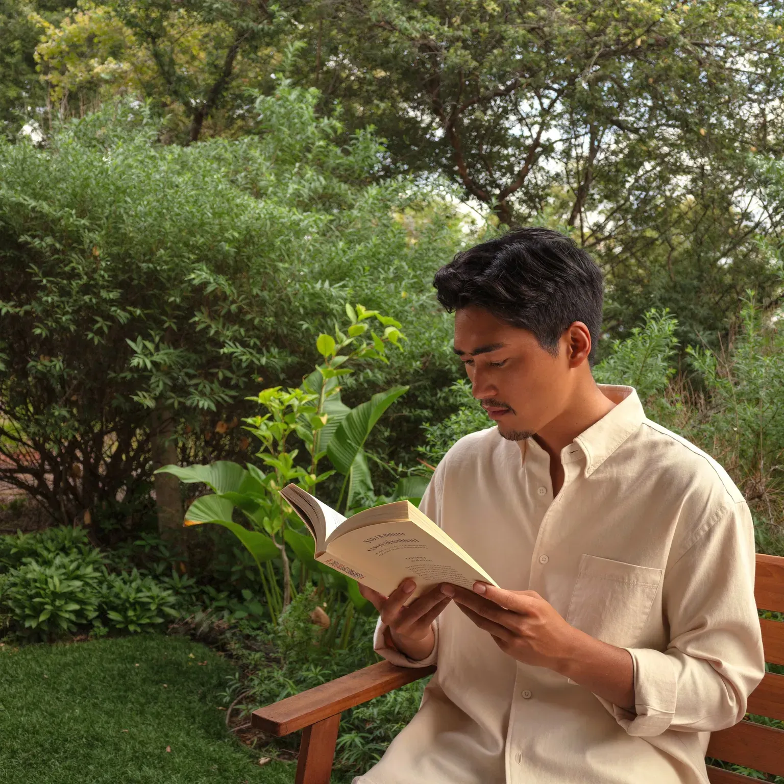 A man reading a book on a garden bench