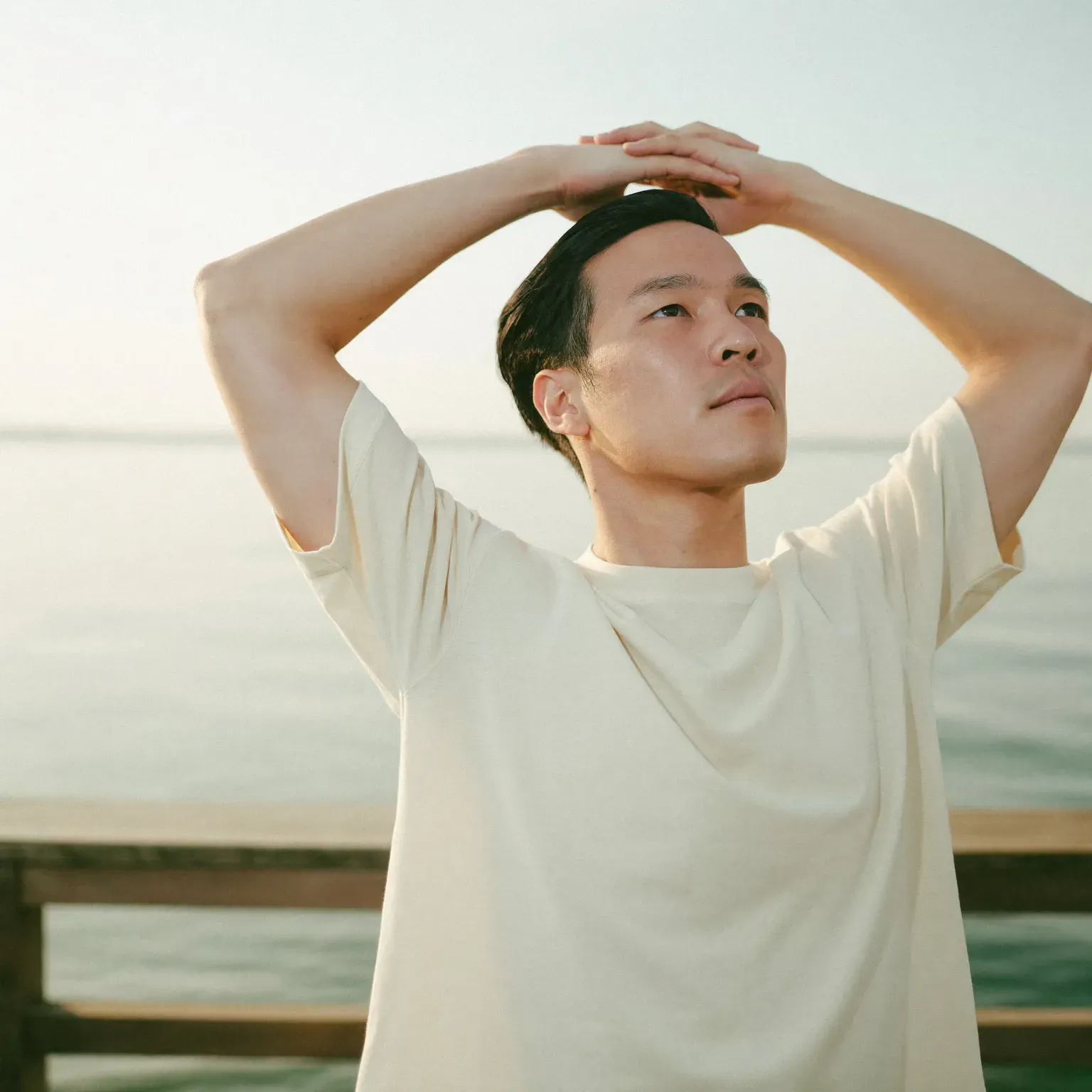 A man with his hands on his head, looking out over water