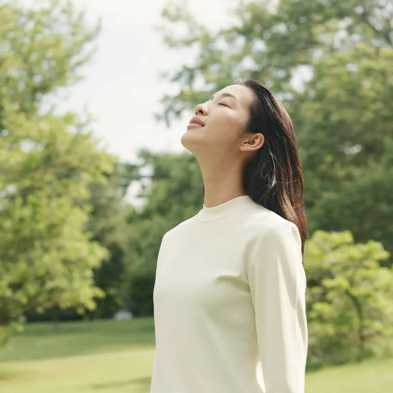A woman with her face turned up to the sky, among trees