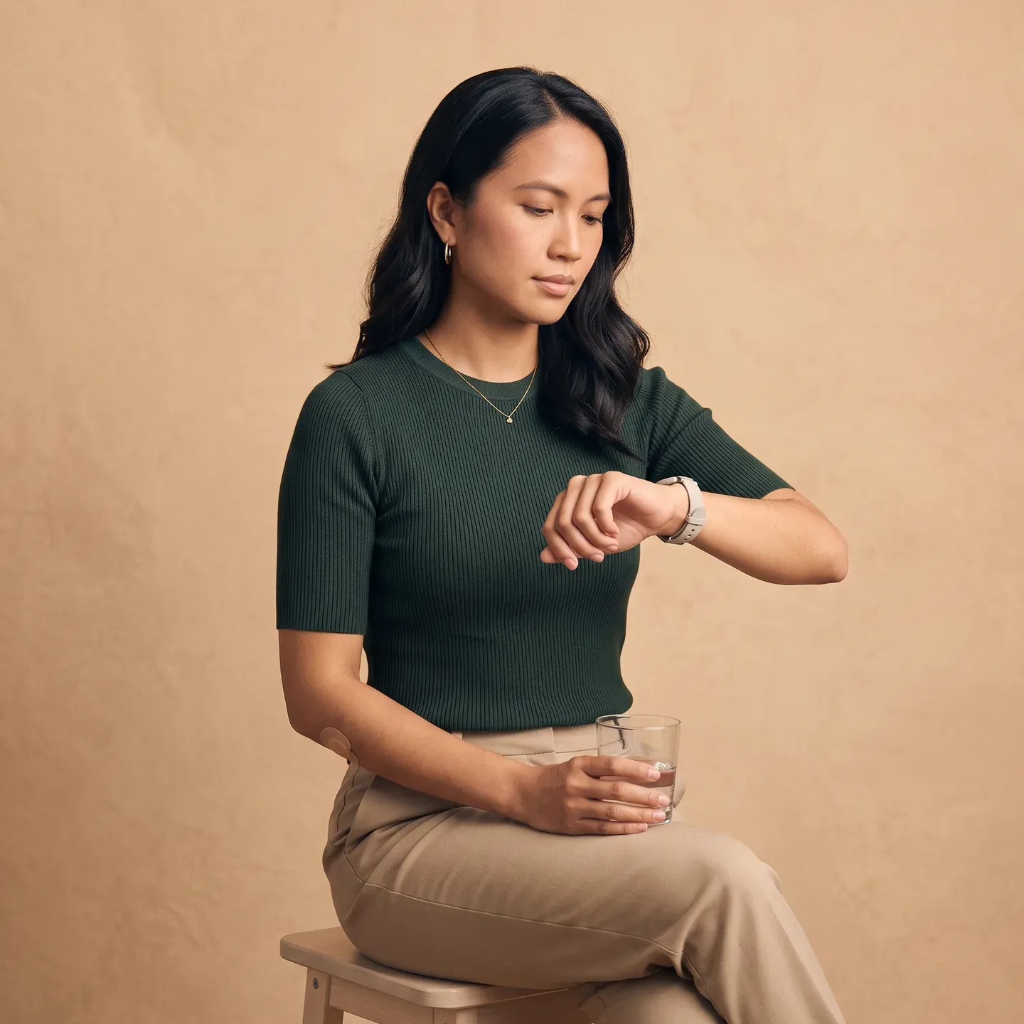 A seated woman checking her watch, a small glass in her other hand