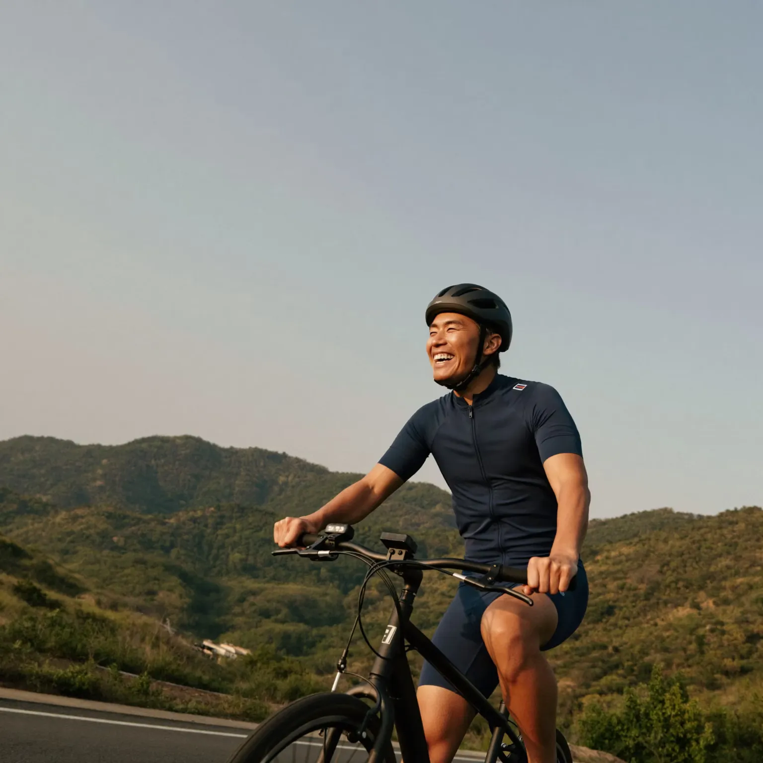 A man smiling as he cycles along a hillside road at dusk