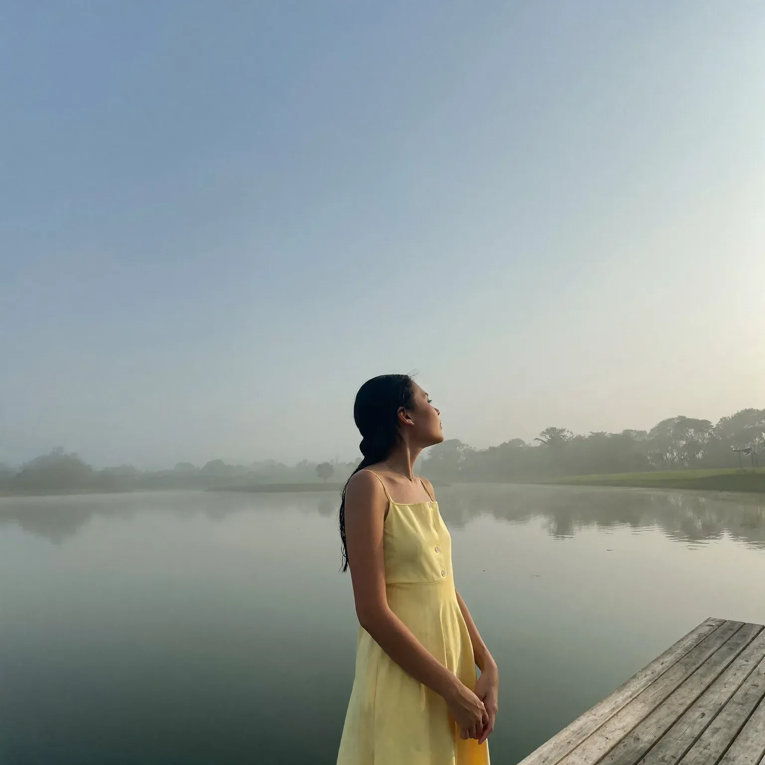 A woman standing on a jetty by a misty lake