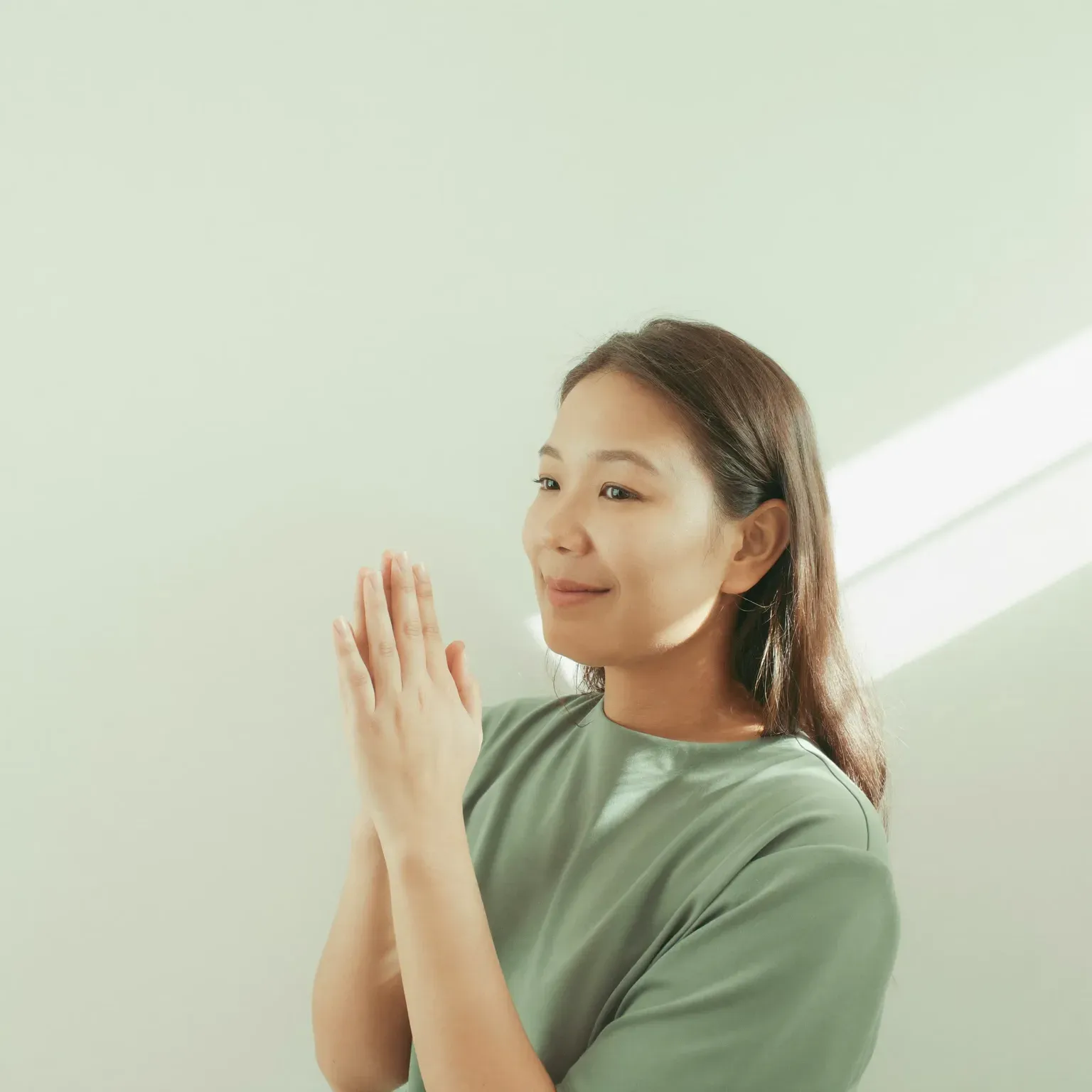 A woman with her hands pressed together beside her face