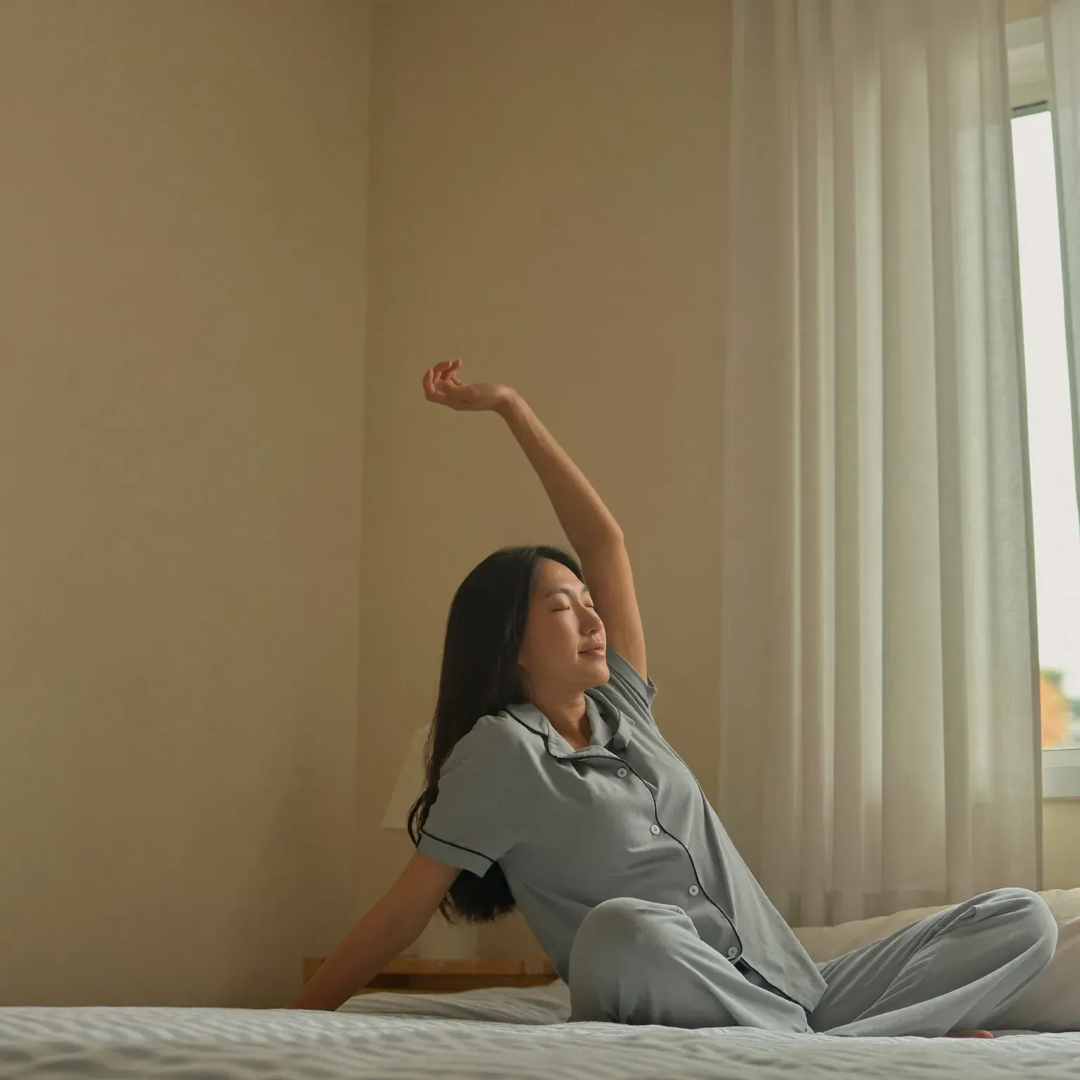 A woman stretching as she wakes, sitting on a bed