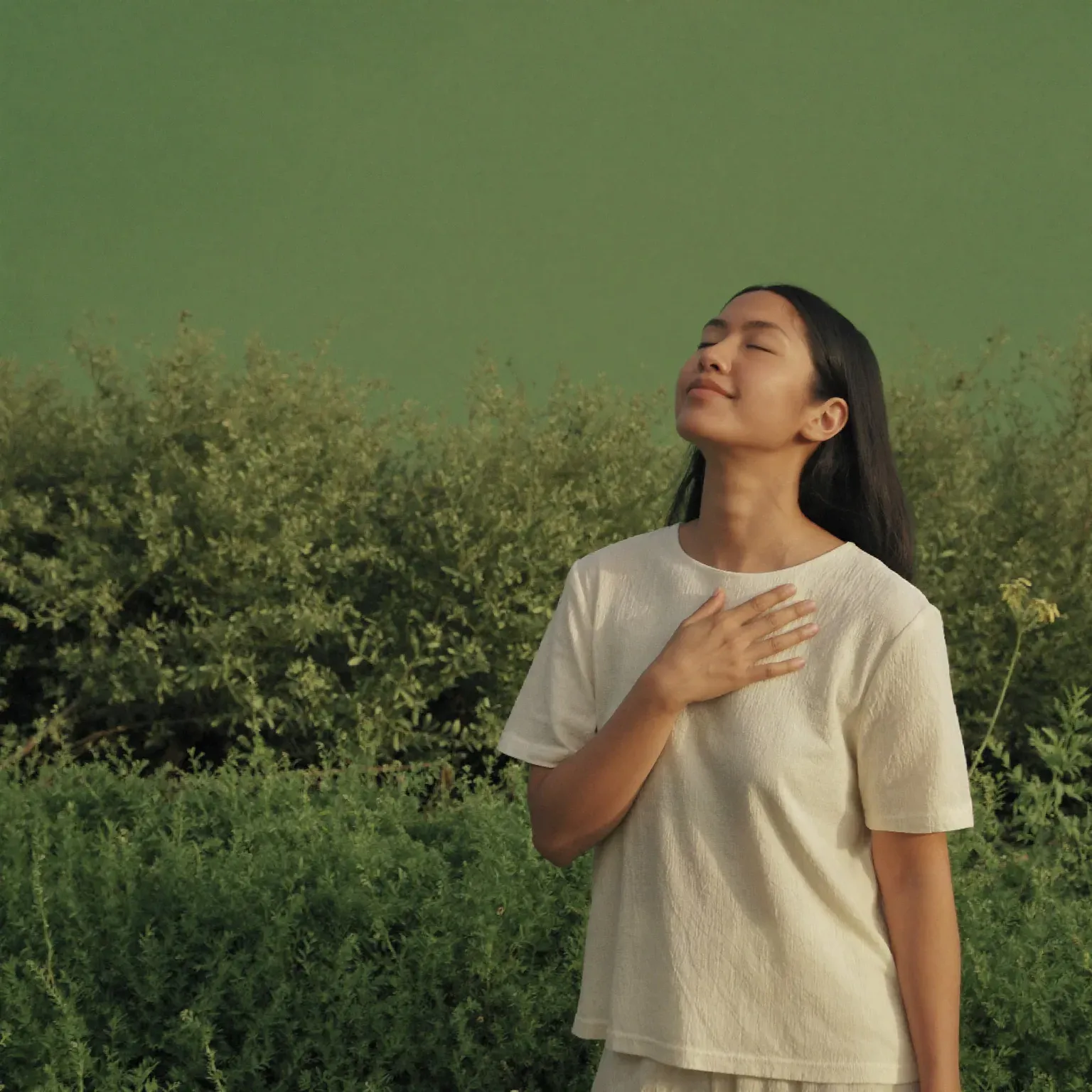 A woman breathing with a hand on her chest and her eyes closed