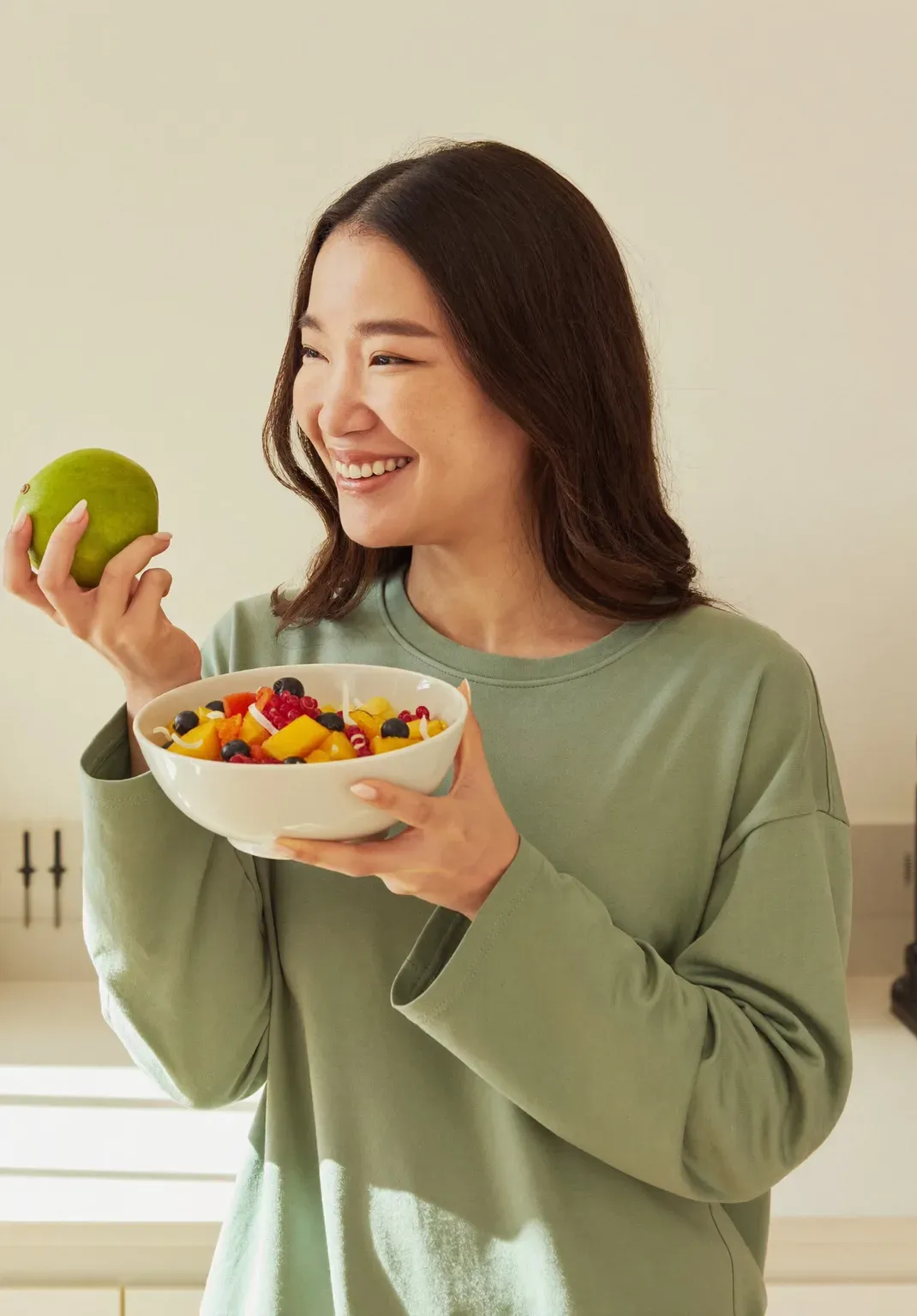 A woman holding a bowl of fruit and a green mango